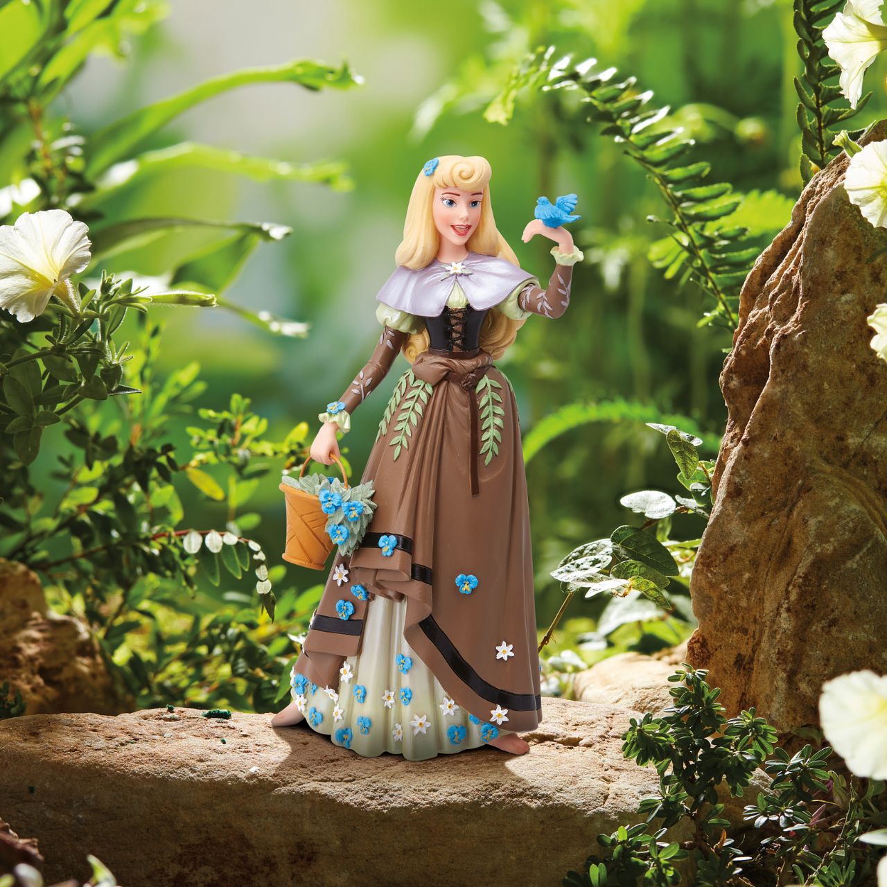 The iconic Disney princess Aurora from Sleeping Beauty is depicted here in her Briar Rose outfit. She has received the botanical treatment with delicate flowers spreading across her dress and spilling out of her basket while a bird perches on her hand.