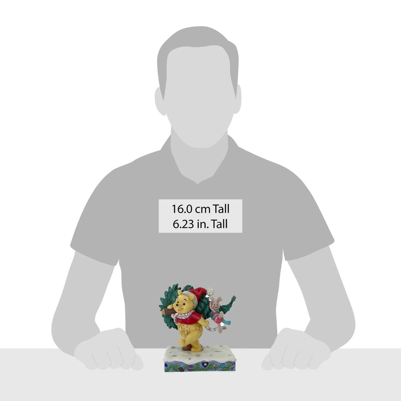 In this delightful Jim Shore scene, Winnie the Pooh sports intricate rosemaling and a Santa hat adorned with holly as he joyfully carries home a Christmas tree with Piglet in tow. They march through the snow on a festive stage of ornaments.