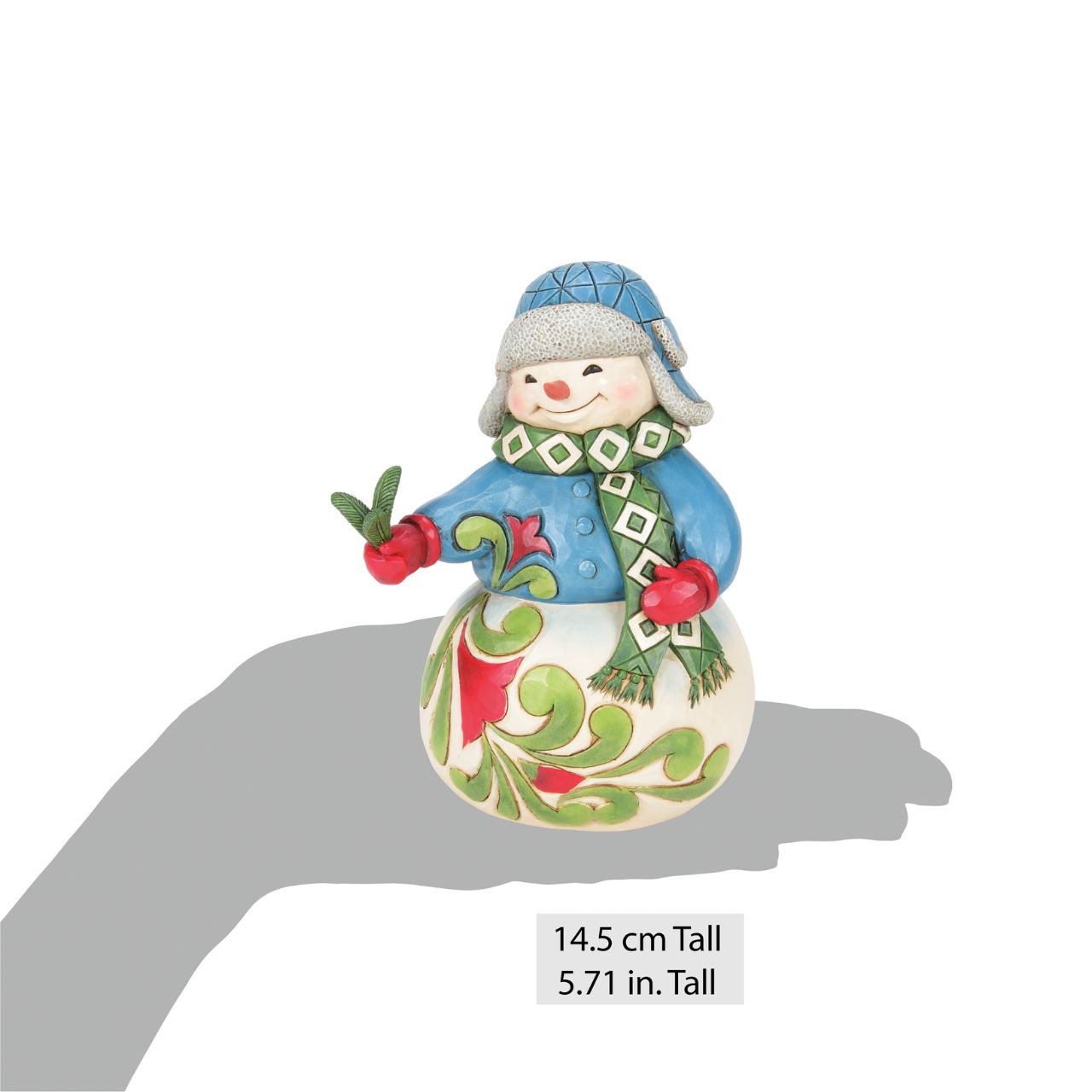 This sweet Jim Shore snowman, adorned in a patterned aviator hat and matching scarf, smiles warmly as he shares a picked pine sprig with you. His body and tunic feature delightful floral designs, adding a touch of charm to your winter decor.