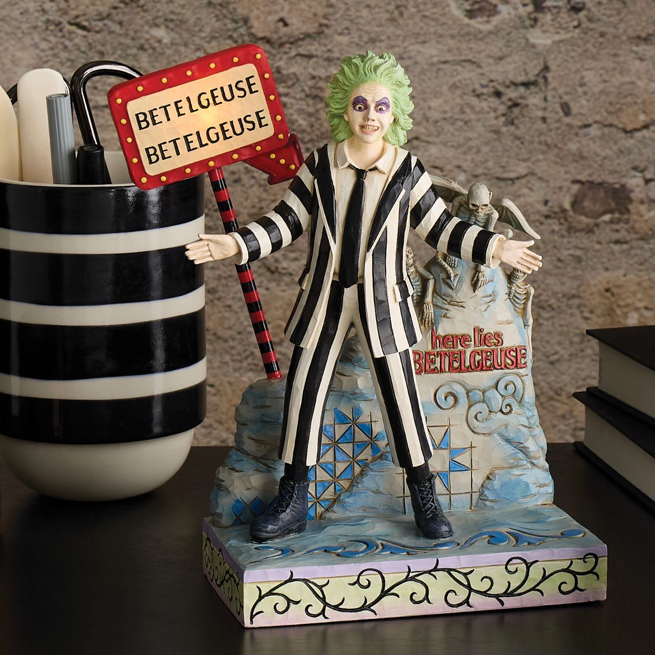 Beetlejuice, Beetlejuice, Beetlejuice... He's here. The iconic bio-exorcist from the 1988 Tim Burton film has arrived and this time, he has a Jim Shore twist. Crafted from high quality cast stone and hand-painted, this light up figurine features the main (dead) man himself, atop his grave with an illuminated "Vegas" style LED sign letting all know who he is.
