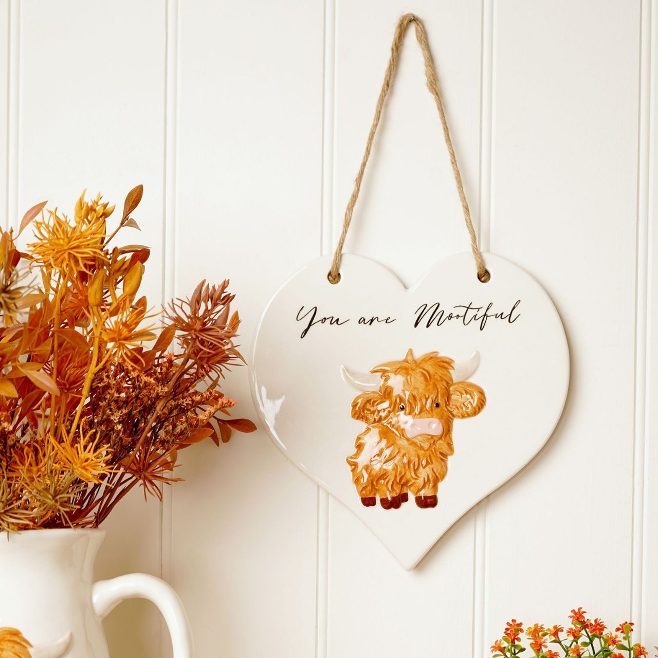 This charming ceramic plaque showcases a whimsical highland cow illustration and the playful message “You are Mootiful”. Shaped like a heart and finished with a rustic rope hanger, it’s cosy design make it a lovely addition to any home.
