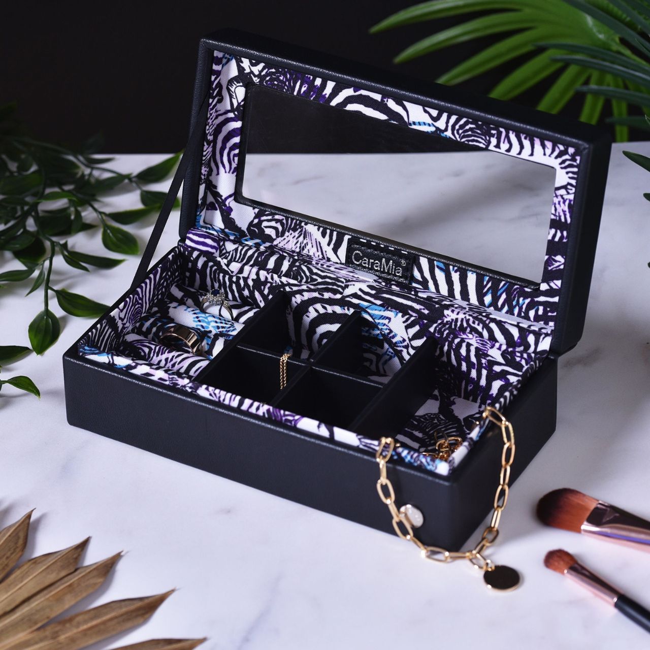 The eye-catching case is made from black faux (vegan) leather, opening to reveal a beautifully decorated storage area with tailor-made compartments for displaying rings, earrings and other jewellery pieces. It is finished with a convenient mirror, within its hinged lid.