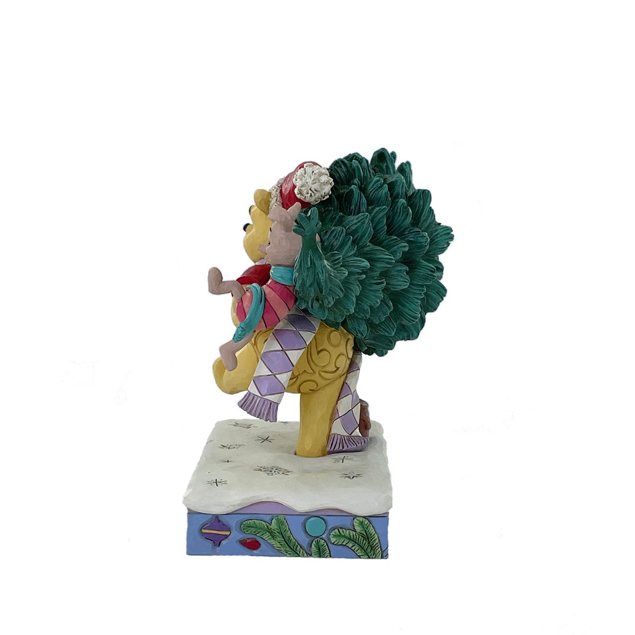 In this delightful Jim Shore scene, Winnie the Pooh sports intricate rosemaling and a Santa hat adorned with holly as he joyfully carries home a Christmas tree with Piglet in tow. They march through the snow on a festive stage of ornaments.
