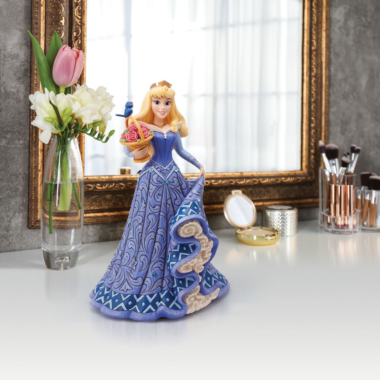 Introducing the Deluxe Aurora Figurine from Disney Traditions by Jim Shore. This exquisite piece depicts Sleeping Beauty Aurora in a beautiful, blue dress, accessorized with a stunning crown, carrying a basket of pink roses with a small bluebird perched on top.