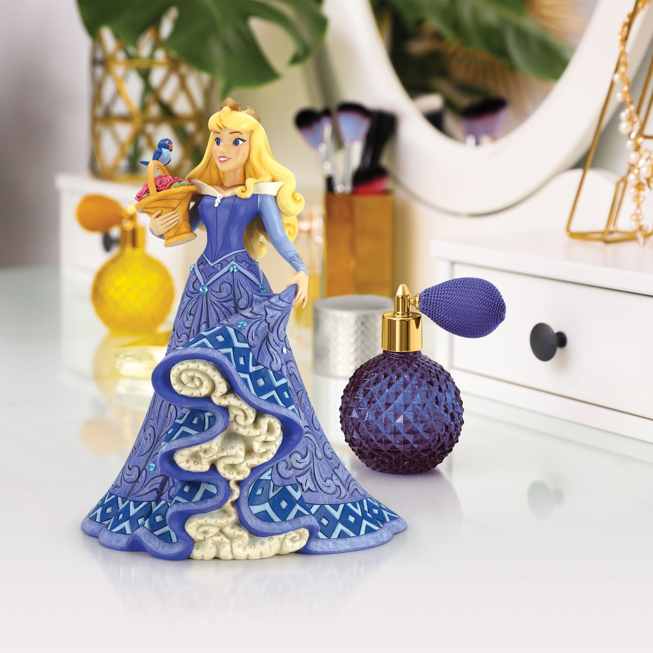Introducing the Deluxe Aurora Figurine from Disney Traditions by Jim Shore. This exquisite piece depicts Sleeping Beauty Aurora in a beautiful, blue dress, accessorized with a stunning crown, carrying a basket of pink roses with a small bluebird perched on top.