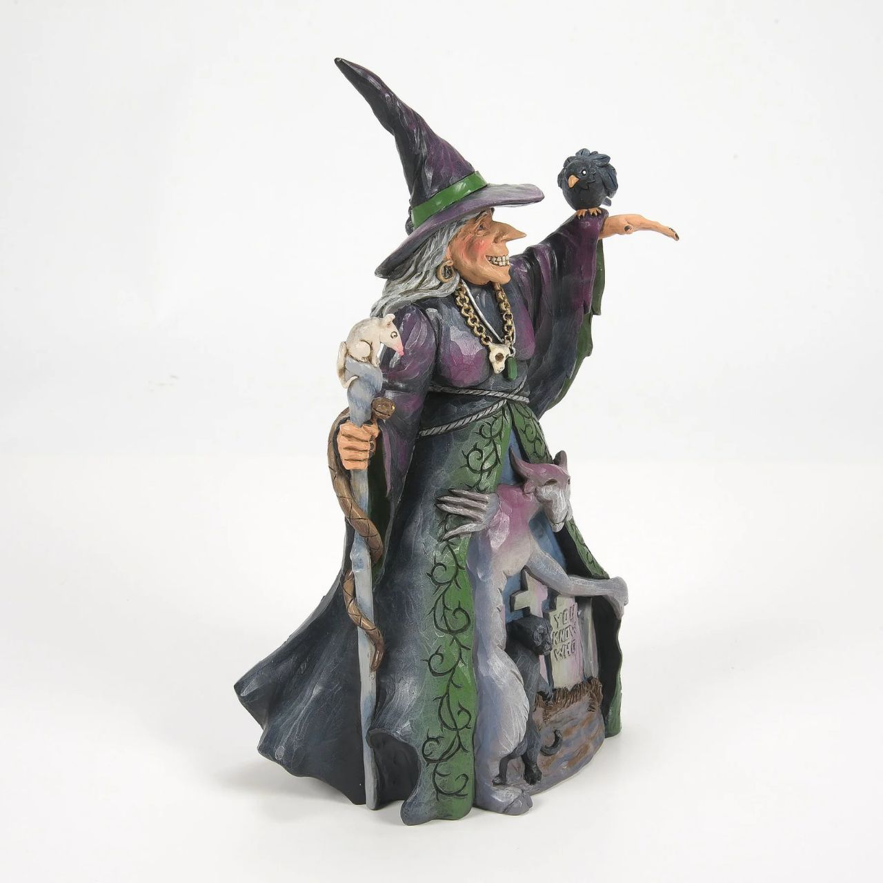 Enter the enchanting world of Halloween with this haunting Jim Shore witch figurine, adorned in ghastly purple and green robes, a perched crow and a staff with a slithering snake. Her cloak reveals a chilling graveyard scene with a spook and a black cat.