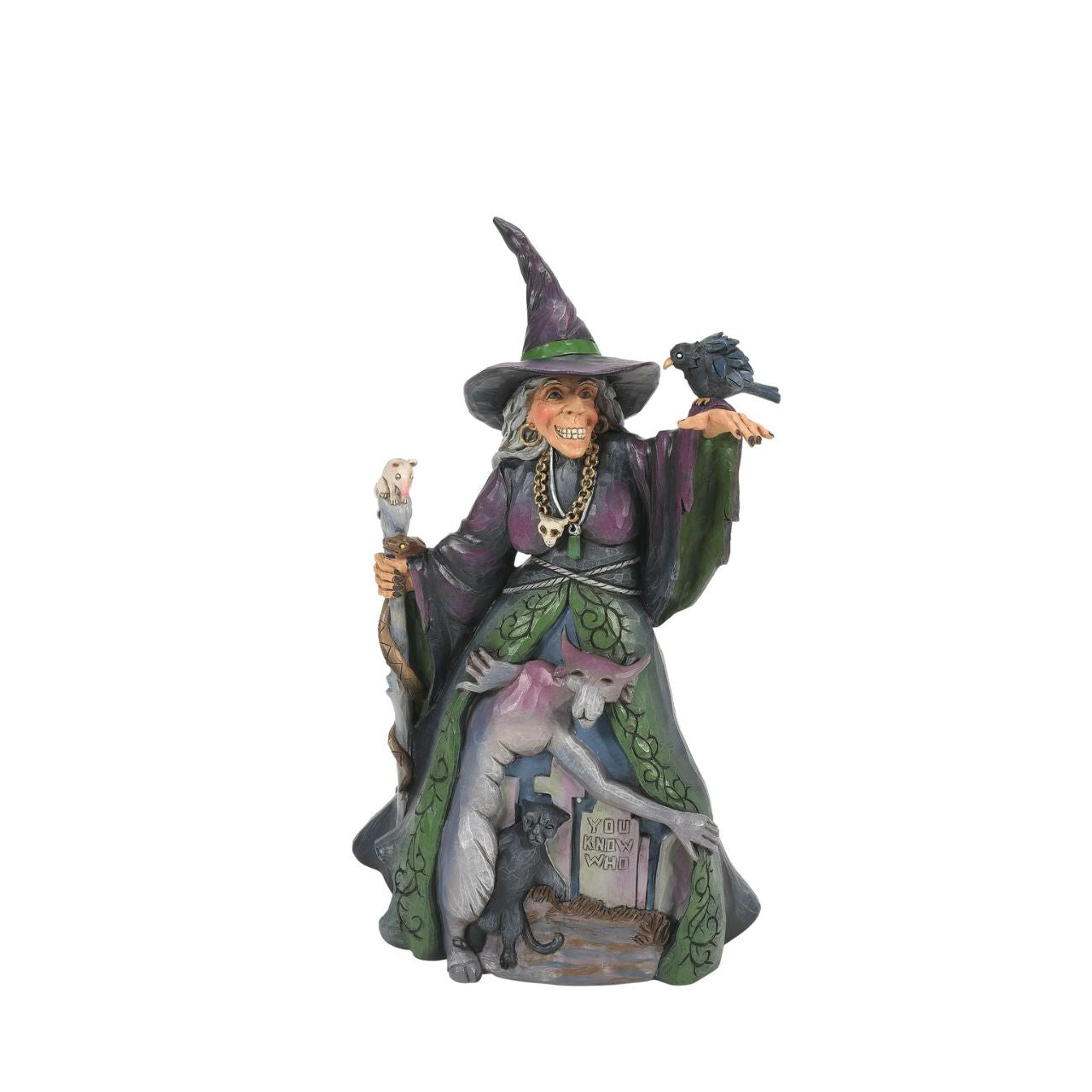 Enter the enchanting world of Halloween with this haunting Jim Shore witch figurine, adorned in ghastly purple and green robes, a perched crow and a staff with a slithering snake. Her cloak reveals a chilling graveyard scene with a spook and a black cat.