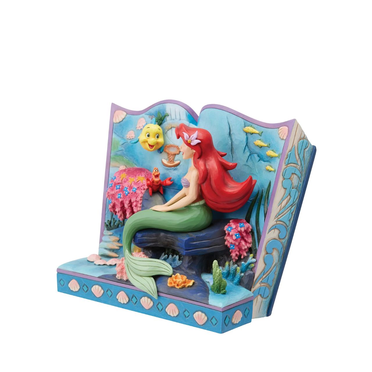 Introducing the Little Mermaid Storybook Figurine from Disney Traditions by Jim Shore. This piece tells the classic tale of Ariel, Flounder, and Sebastian, bringing this beloved story to life in a stunning 3D scene. The figurine depicts Ariel, Flounder, and Sebastian under the sea, surrounded by colourful plant life and shells that add a magical touch to this exquisite work of art.
