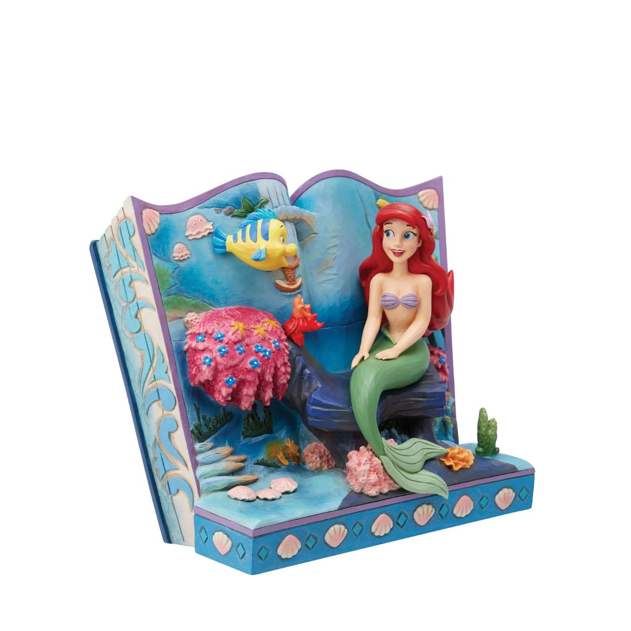 Introducing the Little Mermaid Storybook Figurine from Disney Traditions by Jim Shore. This piece tells the classic tale of Ariel, Flounder, and Sebastian, bringing this beloved story to life in a stunning 3D scene. The figurine depicts Ariel, Flounder, and Sebastian under the sea, surrounded by colourful plant life and shells that add a magical touch to this exquisite work of art.