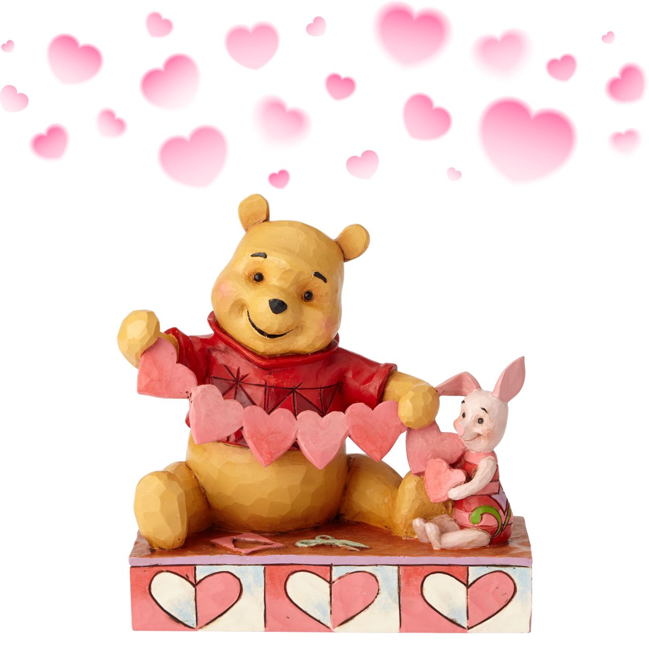 Disney Traditions Handmade Valentines Pooh and Piglet Figurine Will you be Pooh's Valentine? Piglet and Winnie the Pooh sit close beside each other as they trace and snip a handmade garland of hearts. Folk art-inspired details add to the artisanal charm of this hand-painted figurine, sculpted from high-quality cast stone.