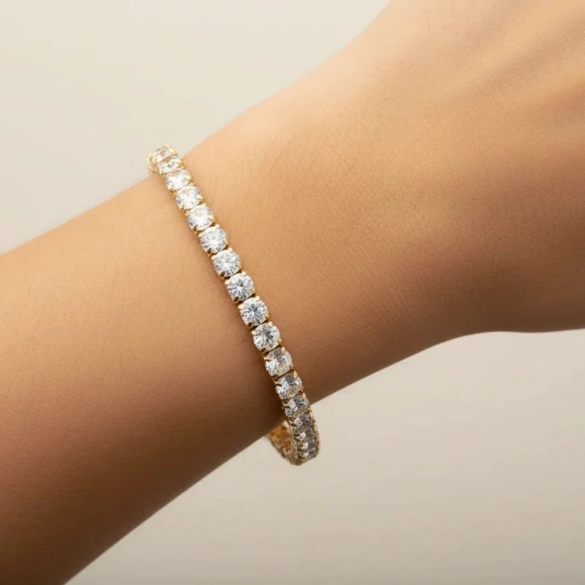 Elegant tennis bracelet featuring a continuous line of sparkling 4mm cubic zirconia stones set in warm gold plating. The classic design offers timeless sophistication for everyday wear or special occasions.