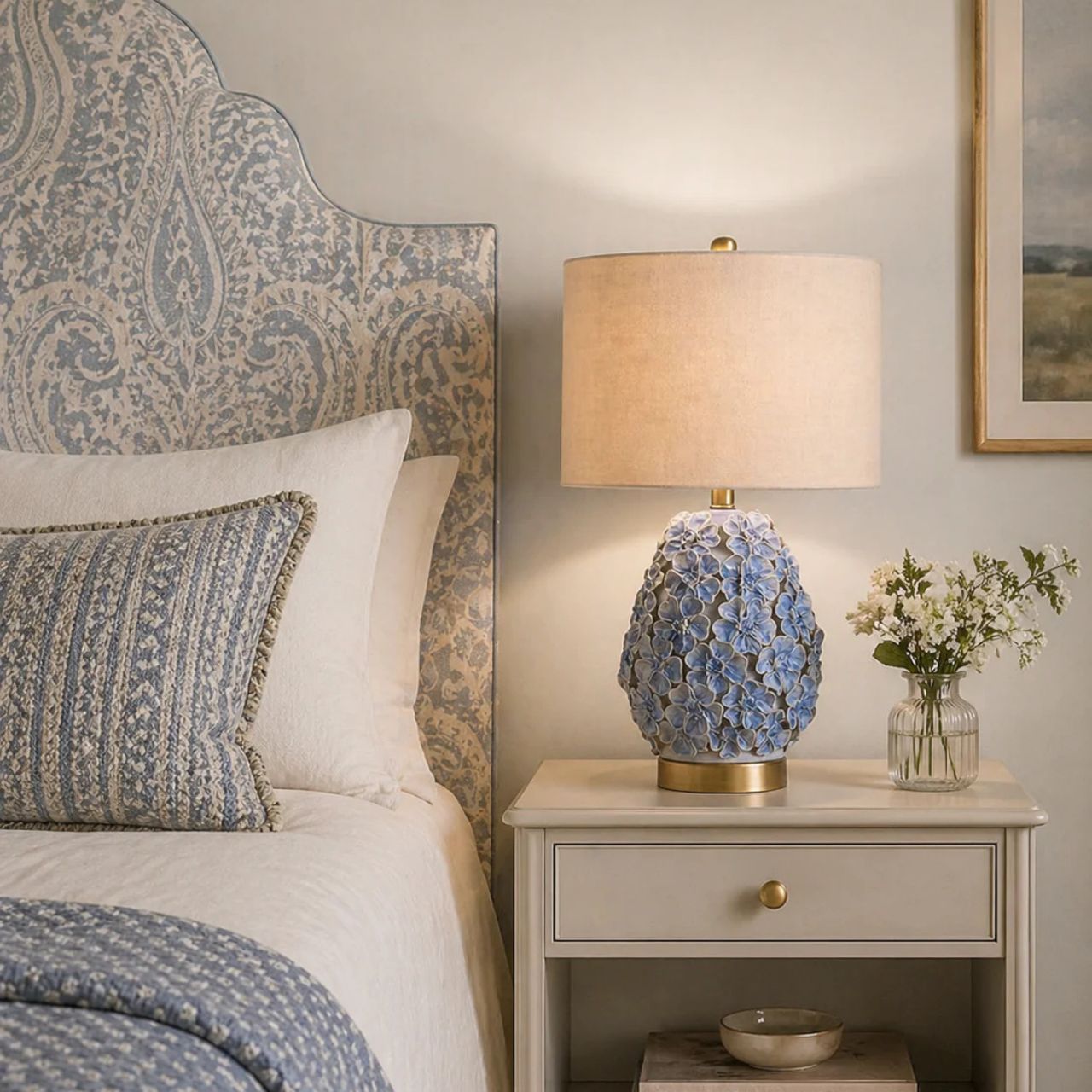 The Olivia Lamp is a charming piece inspired by delicate floral forms. Its rounded ceramic base features softly raised blossoms in gentle blue tones, creating texture and a subtle romantic feel. Finished with a neutral shade, it casts a warm, inviting glow.