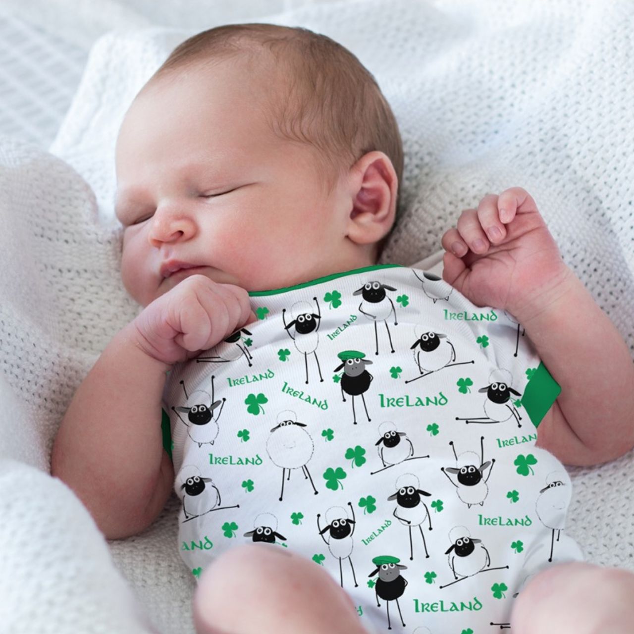 White & Green Overall Printed Sheep Baby Vest This white and green baby vest is part of the Traditional Craft Official Collection. This white cotton vest has an emerald green trim on the neck, sleeves and bottom. The vest is designed with an over all print of sheep, shamrocks & Ireland logo's from the Flaherty Flock range.
