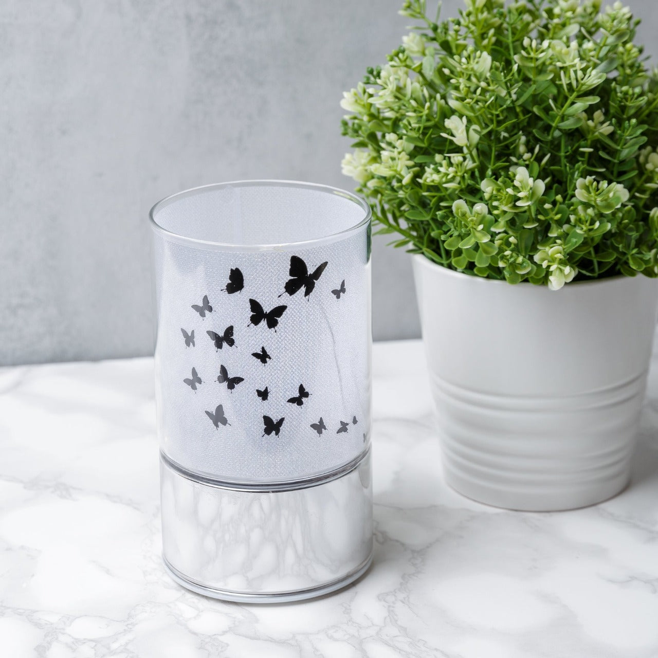 HESTIA® Glass Butterfly Design Tube with LED Lights 15cm A beautiful LED tube from HESTIA®'s Silver Luxe collection. Featuring a dazzling glitter finish with butterfly design on a metal base. Requires 3 x AA batteries for use.
