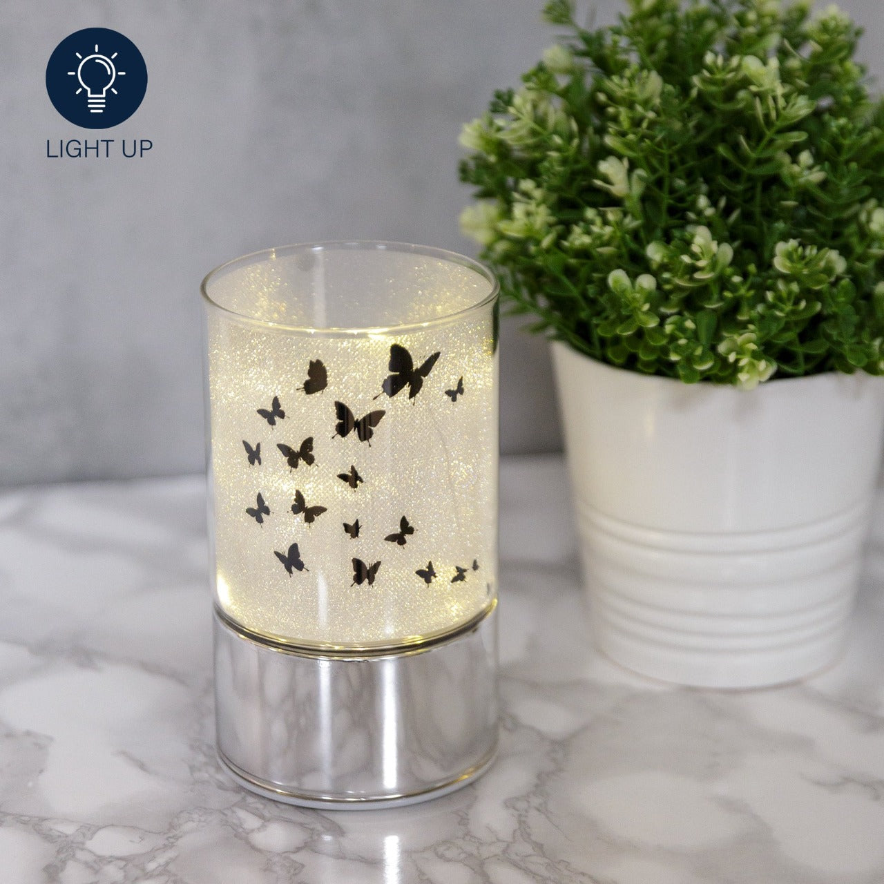 HESTIA® Glass Butterfly Design Tube with LED Lights 15cm A beautiful LED tube from HESTIA®'s Silver Luxe collection. Featuring a dazzling glitter finish with butterfly design on a metal base. Requires 3 x AA batteries for use.
