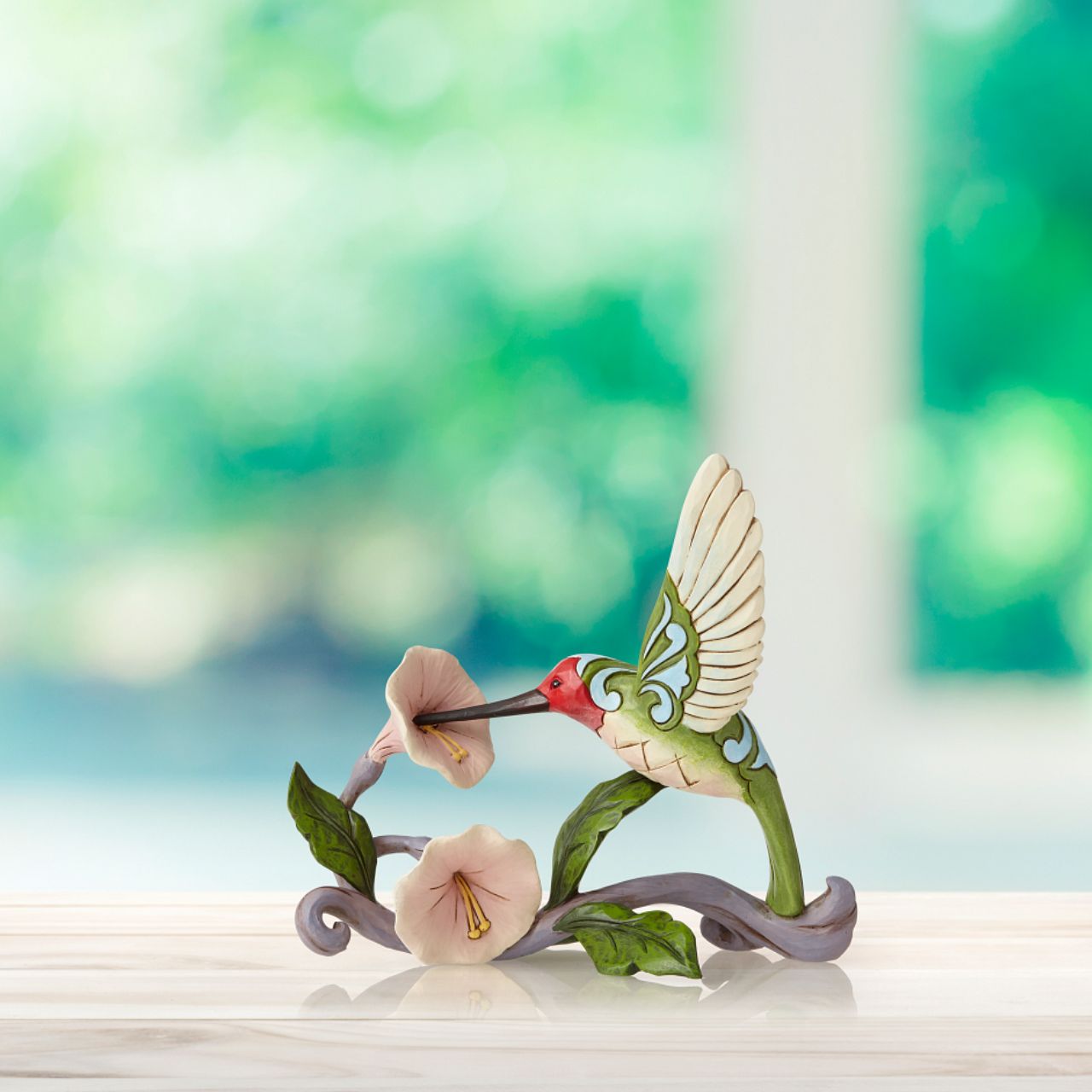 Jim Shore Heartwood Creek Blossoms and Beauty - Hummingbird with Flower  A colourful accent to brighten your day, Jim Shore's richly detailed Hummingbird design features a combination of subtle quilt patterning and beautifully hand-crafted rosemaling motifs. Each Heartwood Creek piece is hand painted, crafted using high quality cast stone. Comes in a branded Kraft gift box.
