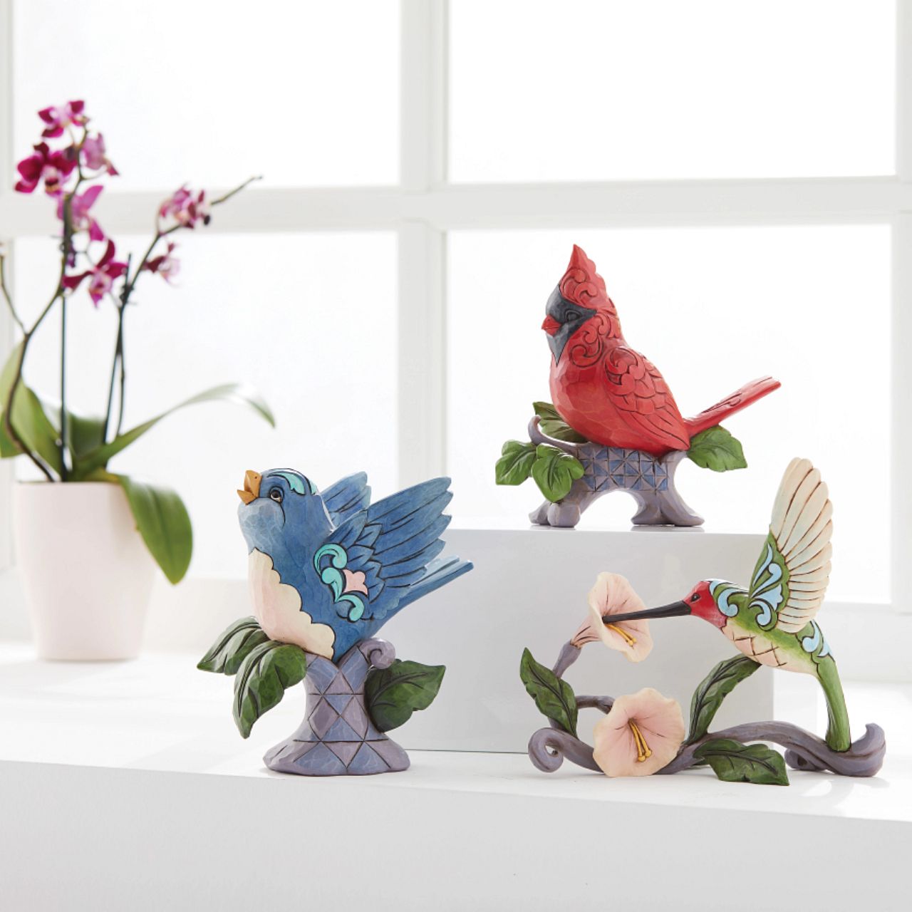 Jim Shore Heartwood Creek Blossoms and Beauty - Hummingbird with Flower  A colourful accent to brighten your day, Jim Shore's richly detailed Hummingbird design features a combination of subtle quilt patterning and beautifully hand-crafted rosemaling motifs. Each Heartwood Creek piece is hand painted, crafted using high quality cast stone. Comes in a branded Kraft gift box.