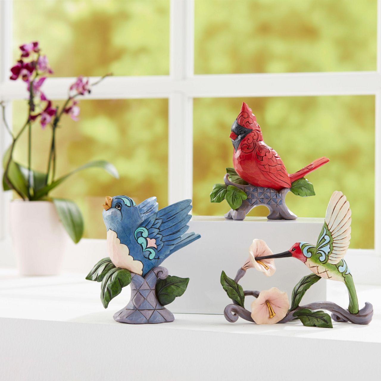 Jim Shore Heartwood Creek Blossoms and Beauty - Hummingbird with Flower  A colourful accent to brighten your day, Jim Shore's richly detailed Hummingbird design features a combination of subtle quilt patterning and beautifully hand-crafted rosemaling motifs. Each Heartwood Creek piece is hand painted, crafted using high quality cast stone. Comes in a branded Kraft gift box.