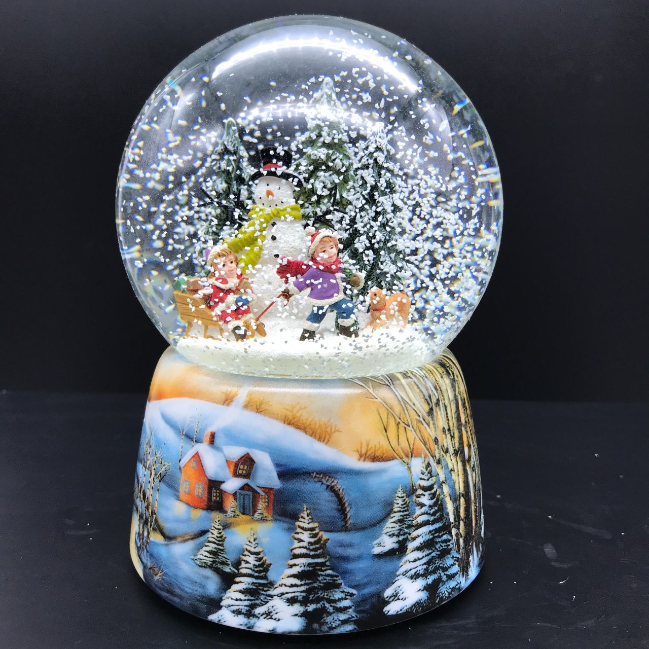 Music Box World Snow Globe Building a Snowman  Snow globe build a snowman. In the ball full of snow, two children with their sled pass by their snowman. Small snowy pine trees decorate the scene. The base is painted with snow-covered forest and village scenes.