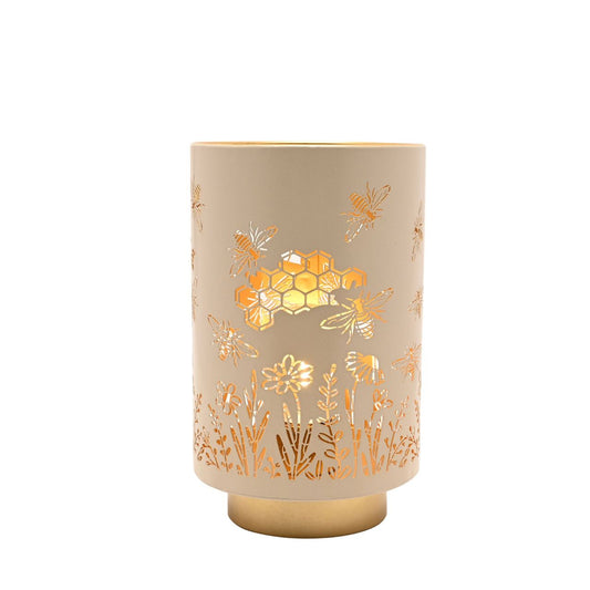 A decorative LED table lamp featuring delicate bee, honeycomb, and floral cut-out detailing. The soft neutral finish paired with warm gold accents creates a cosy, nature-inspired look.