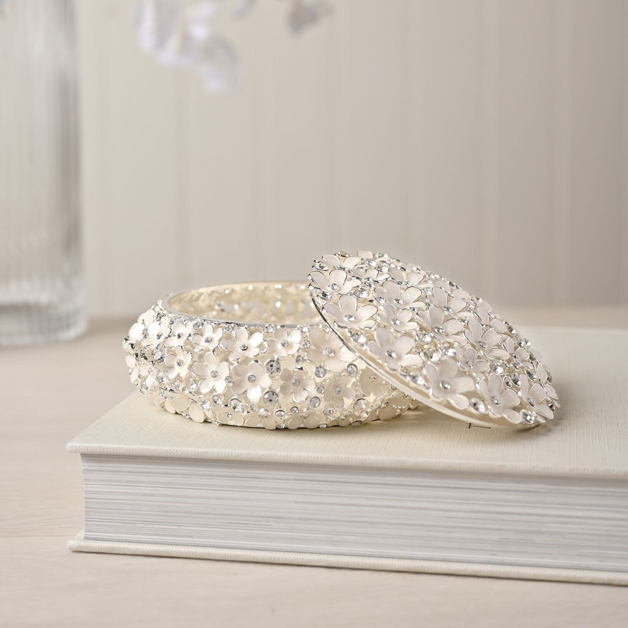 Indulge in the decadence of the Sophia Classic Daisy Open Work Trinket Box, a resplendent round piece adorned with shimmering crystals. This ornate jewel box, set against a crisp white backdrop, is an exquisite addition to any dressing table, radiating a unique charm.