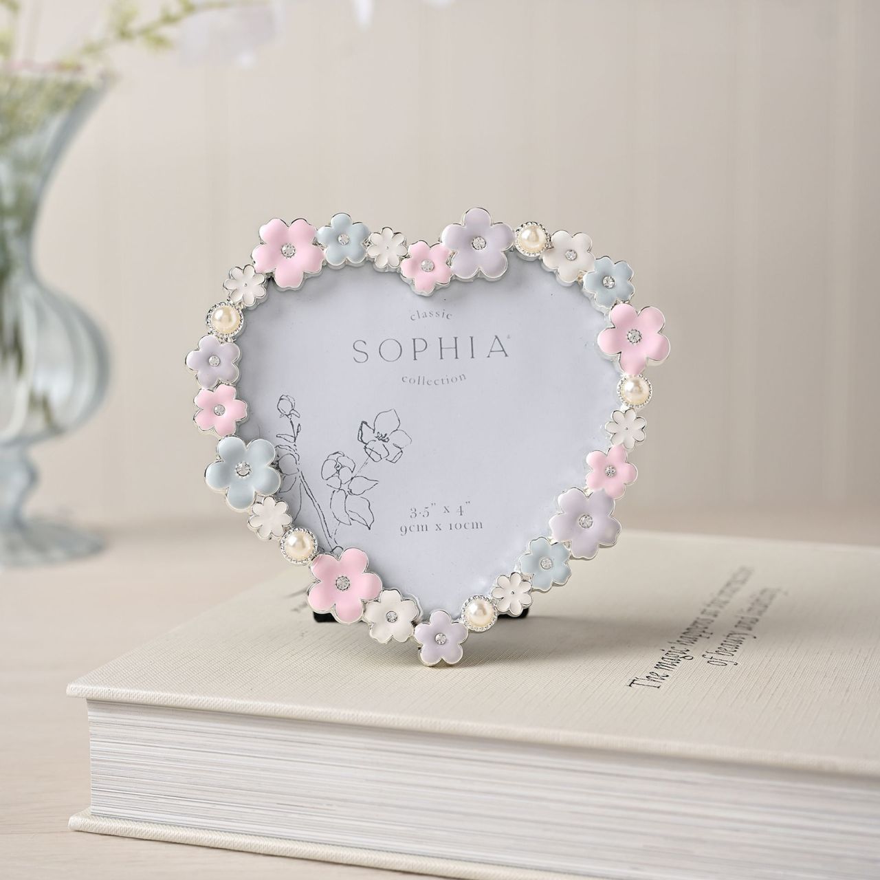Make your memories bloom with the Sophia Classic Daisy 4 x 6 Heart Frame in Pastel. This heart-shaped frame, adorned with delicate white and pink flowers, offers a charming home for your cherished photos, adding pastel charm to any decor.