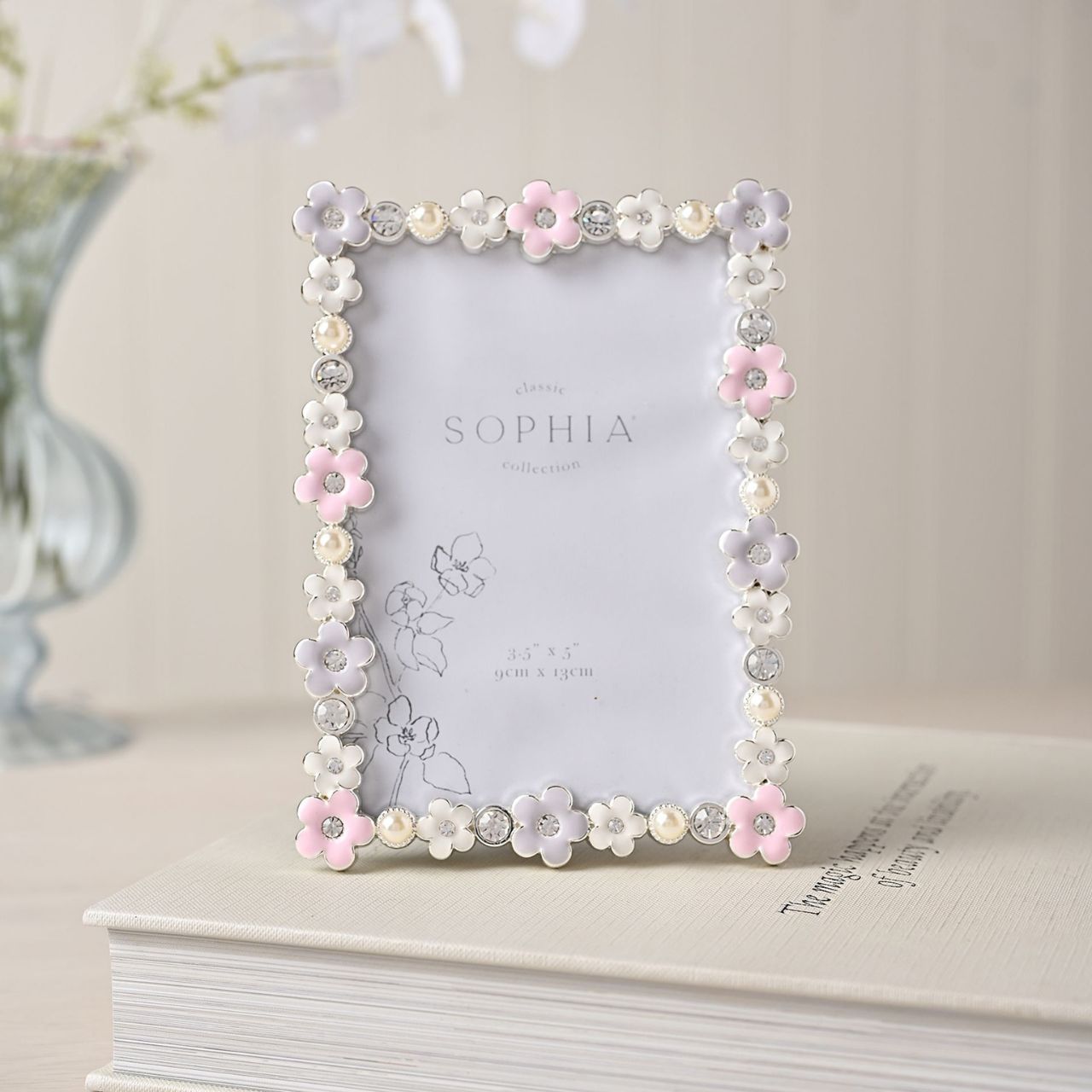 Introducing the Sophia Classic Daisy 3.5" x 5" Frame - Pastel, a delightfully charming piece that pairs perfectly with precious memories. Adorned with delicate white and pink flowers, it’s a treat for the eyes, while sparkling rhinestones add glamour.