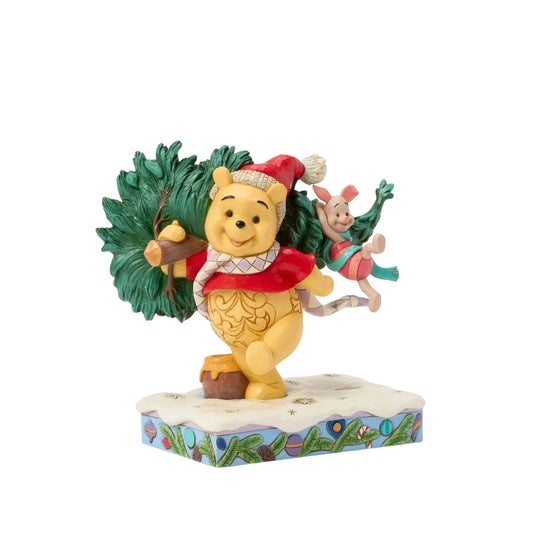 In this delightful Jim Shore scene, Winnie the Pooh sports intricate rosemaling and a Santa hat adorned with holly as he joyfully carries home a Christmas tree with Piglet in tow. They march through the snow on a festive stage of ornaments.