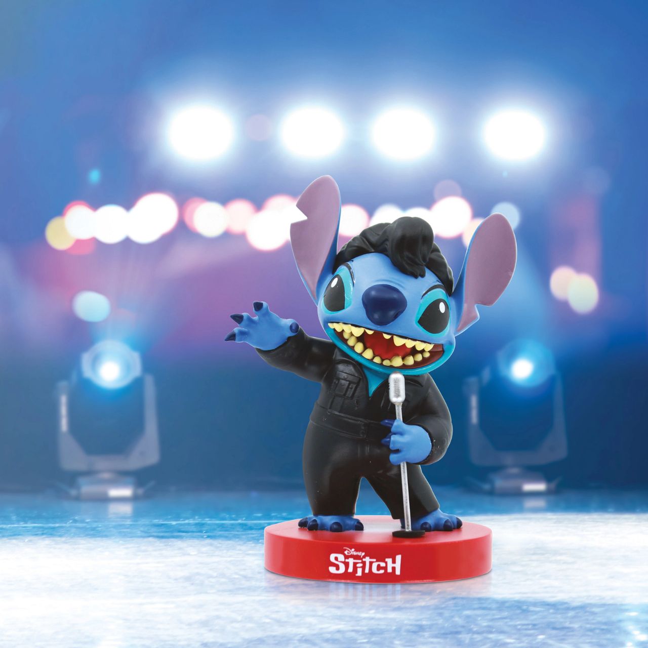 Stitch figurine in a superhero costume on a red base with blurred lights in the background