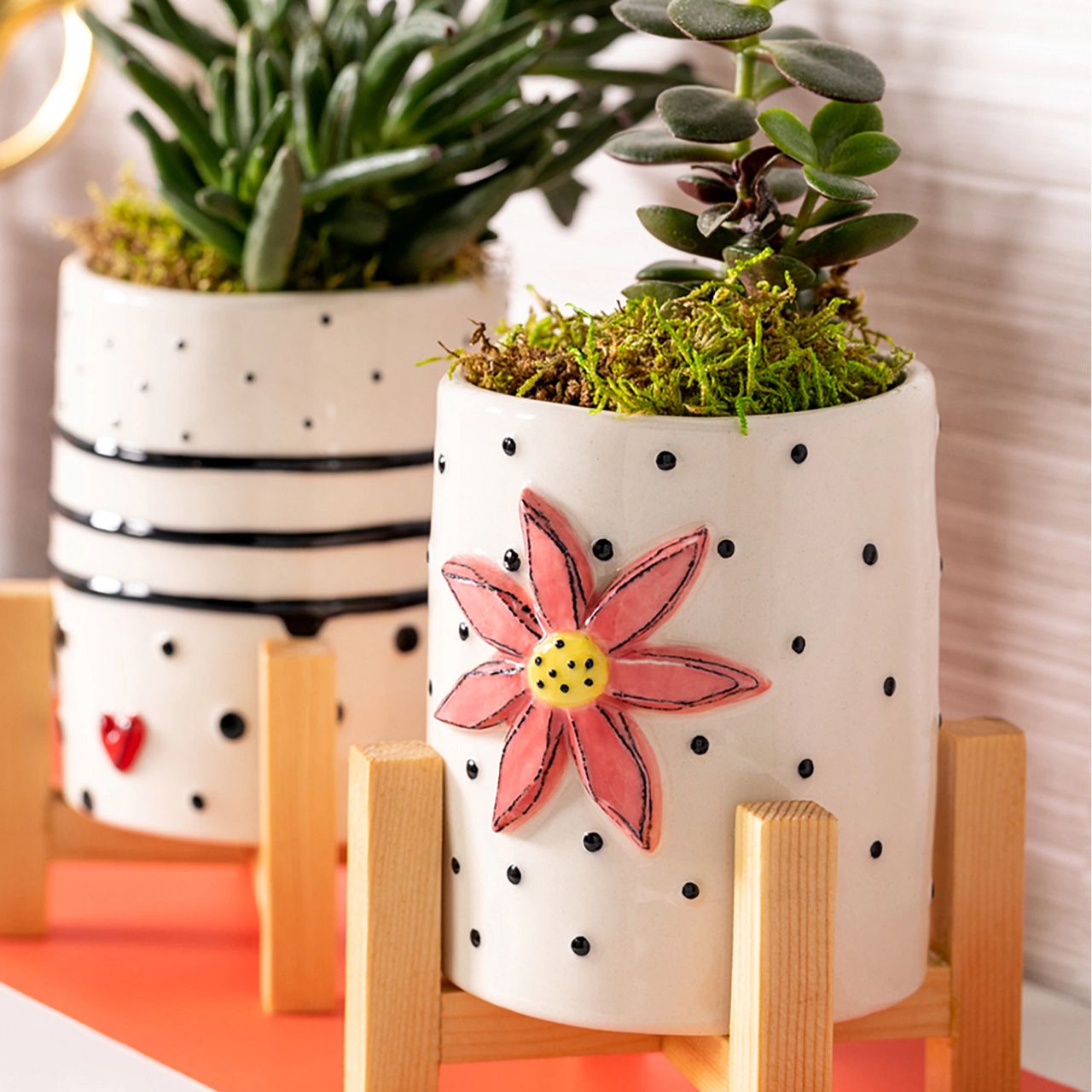 Tracy Pesche's Flower Mini Planter  Add a whimsical, happy touch to your home with Tracy Pesche's uplifting ceramic art. Her hand-painted Flower Mini Planter is a white planter with black polka dots and a bold pink Flower. The light wood base makes the planter sturdy and perfect for many decorating styles.