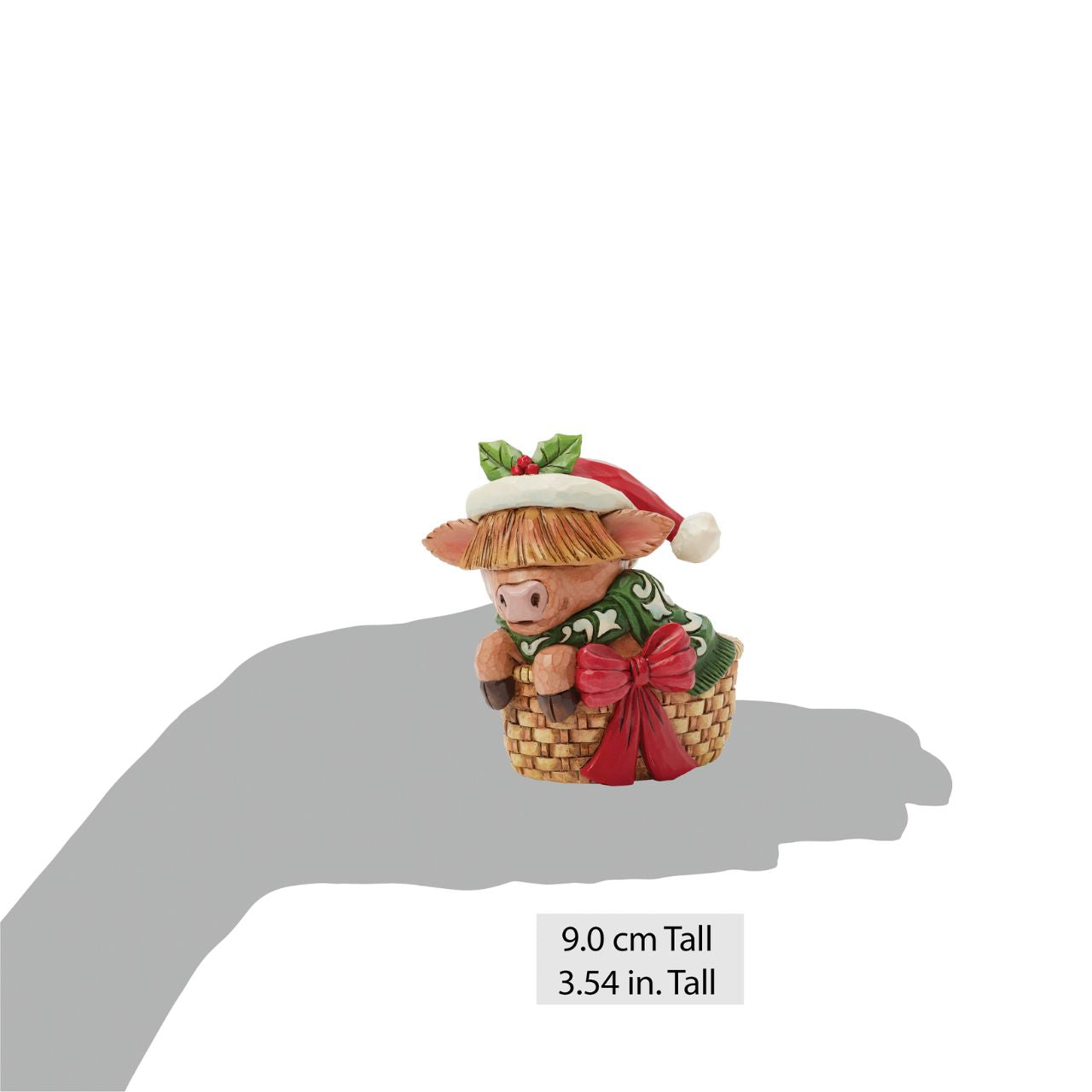 This adorable Jim Shore highland cow miniature radiates holiday cheer from within a cozy basket adorned with a festive bow. Dressed in a cheerful scarf and a Santa hat trimmed with holly, this delightful piece brings warmth and whimsy to your home.