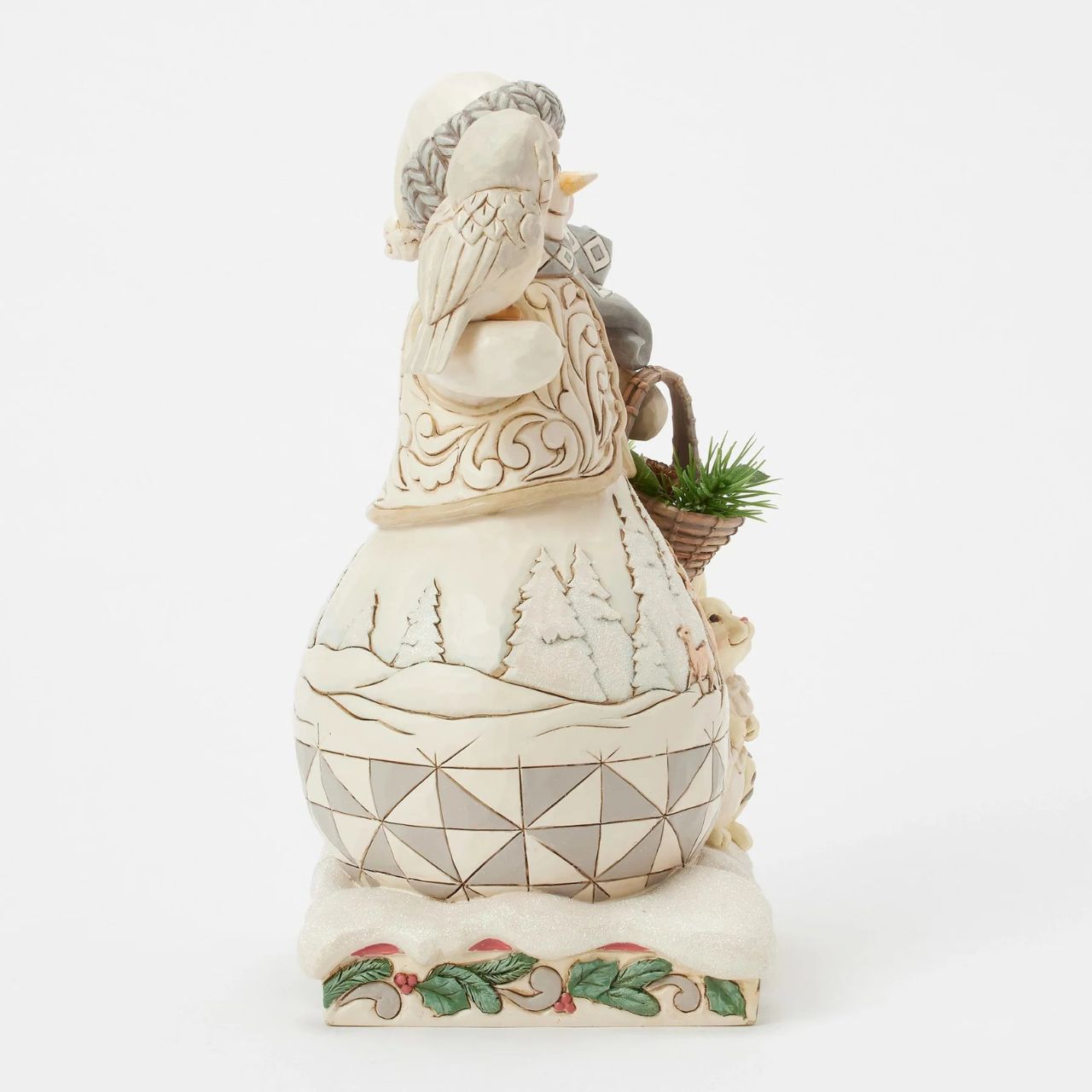 This enchanting Jim Shore White Woodland design features a charming snowman collecting evergreen sprigs in a basket, accompanied by a wise owl and a rabbit as he strolls through the serene forest. A deer scene is showcased on beneath his regal vest.