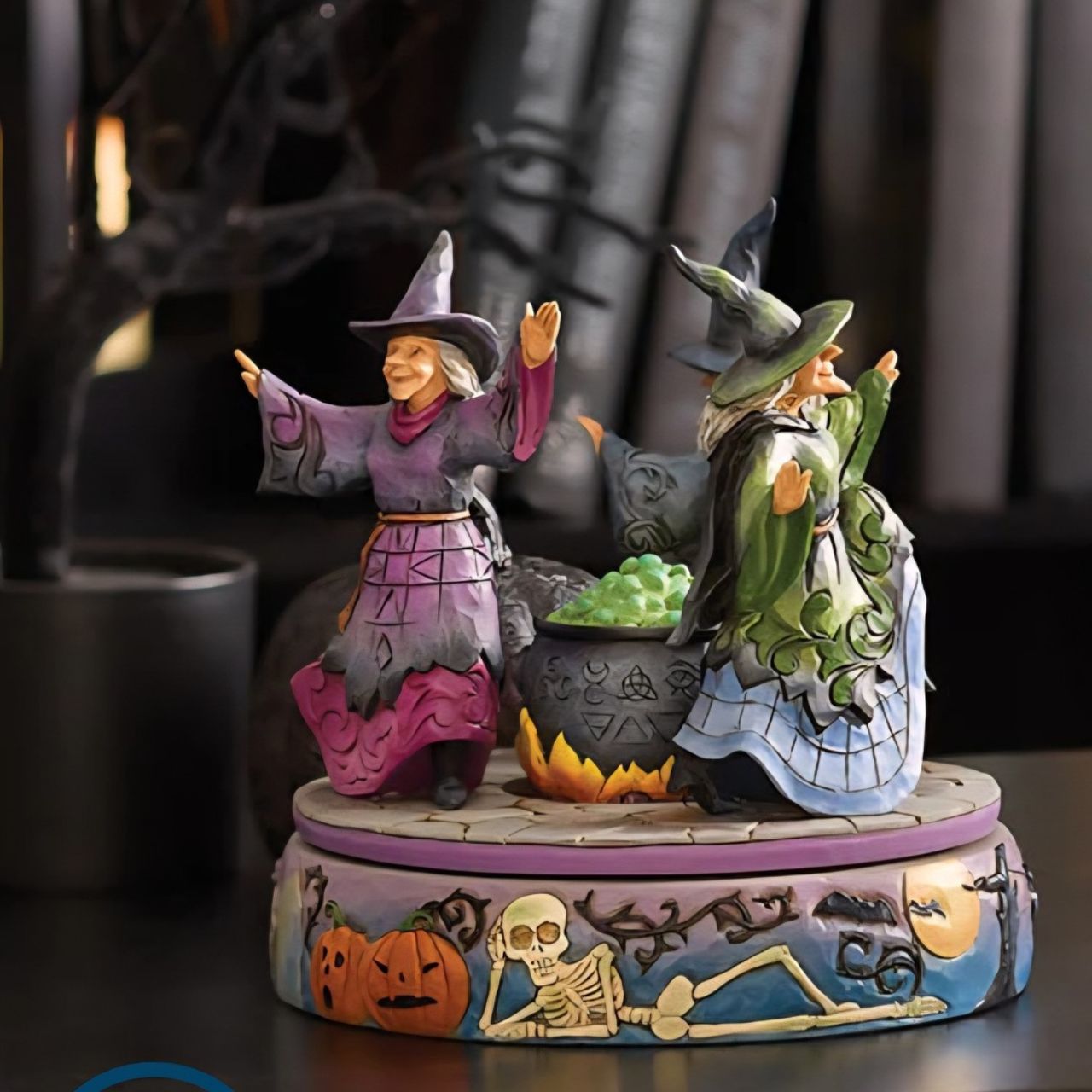 Enter the world of Halloween with this hand-touch rotation Jim Shore movement figurine featuring two witches dancing around a bubbling cauldron. Adorned with jack-o-lanterns, skeletons, tombstones, spiders, snakes, black cats, and bats, it's a bewitching scene.
