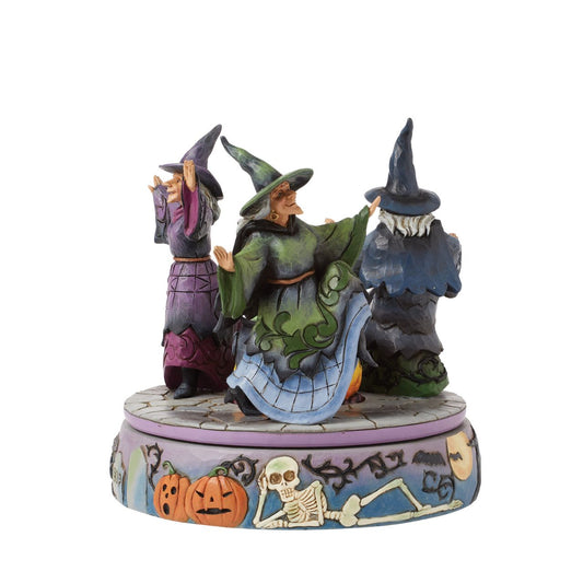 Enter the world of Halloween with this hand-touch rotation Jim Shore movement figurine featuring two witches dancing around a bubbling cauldron. Adorned with jack-o-lanterns, skeletons, tombstones, spiders, snakes, black cats, and bats, it's a bewitching scene.