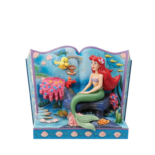 Introducing the Little Mermaid Storybook Figurine from Disney Traditions by Jim Shore. This piece tells the classic tale of Ariel, Flounder, and Sebastian, bringing this beloved story to life in a stunning 3D scene. The figurine depicts Ariel, Flounder, and Sebastian under the sea, surrounded by colourful plant life and shells that add a magical touch to this exquisite work of art.