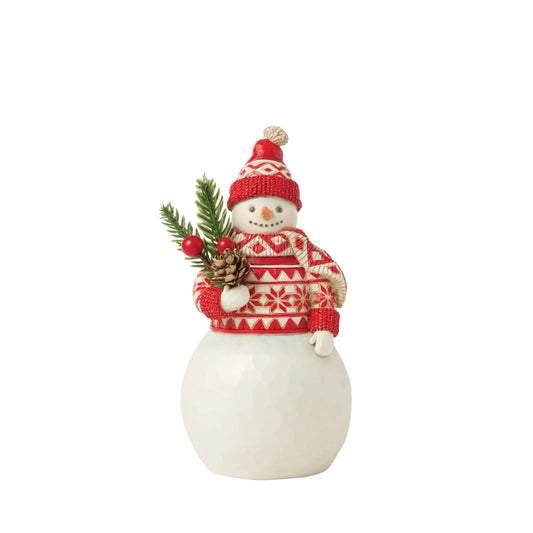 This cheerful Jim Shore Nordic Noel snowman is dressed in an intricately patterned red Nordic sweater, scarf, and hat, radiating warmth and holiday spirit. With a bright smile, he holds a fresh evergreen sprig in his hands, eagerly embracing the joys of Christmas.