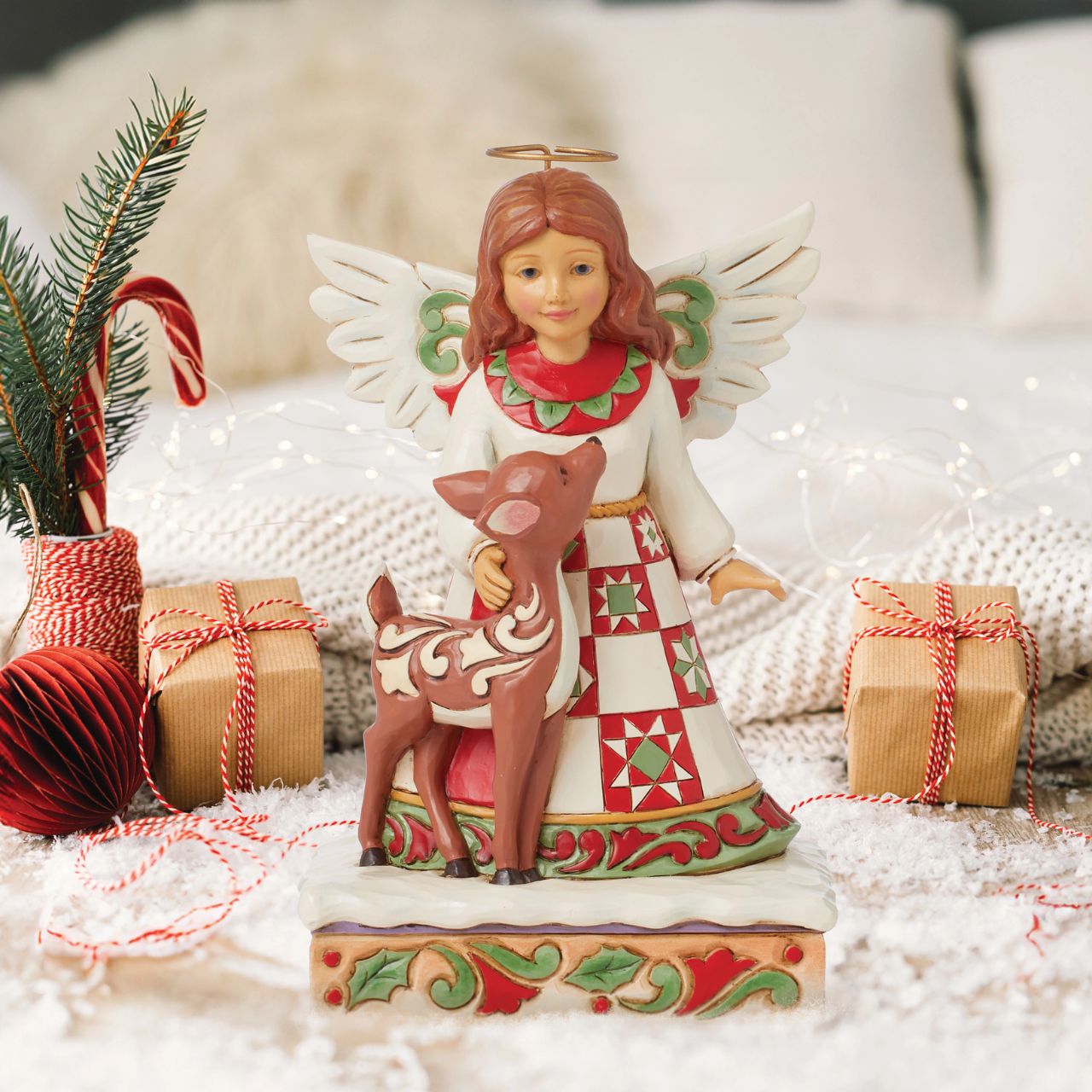 On a stage of flowers, a hallowed angel wears a red and green patchwork patterned dress with a smile. She pats a gentle fawn with a rosemaling pattern. The sweet Jim Shore modelled pair celebrate the simplicity of friendship and miracle of nature.