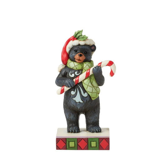 This playful Christmas at the Lodge Jim Shore black bear wears a festive Santa hat adorned with holly, he wears a festive scarf and holds a candy cane in his paws. With rosemaling designs on his fur, the piece brings sweet holiday fun and rustic charm to to any display.