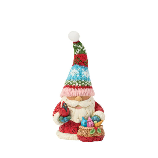 This festive Jim Shore gnome dons a knit holiday hat patterned with snowflakes and Christmas colours, bringing a cosy, inviting texture. Carrying a bag full of ornaments and gently holding a cardinal, he brings holiday cheer to your home.