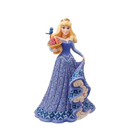 Introducing the Deluxe Aurora Figurine from Disney Traditions by Jim Shore. This exquisite piece depicts Sleeping Beauty Aurora in a beautiful, blue dress, accessorized with a stunning crown, carrying a basket of pink roses with a small bluebird perched on top.