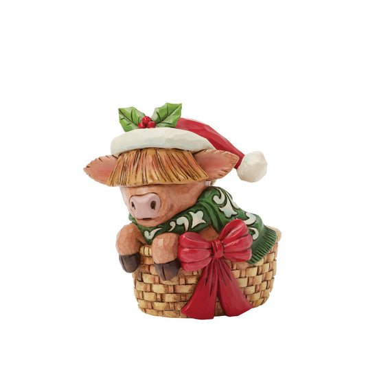 This adorable Jim Shore highland cow miniature radiates holiday cheer from within a cozy basket adorned with a festive bow. Dressed in a cheerful scarf and a Santa hat trimmed with holly, this delightful piece brings warmth and whimsy to your home.
