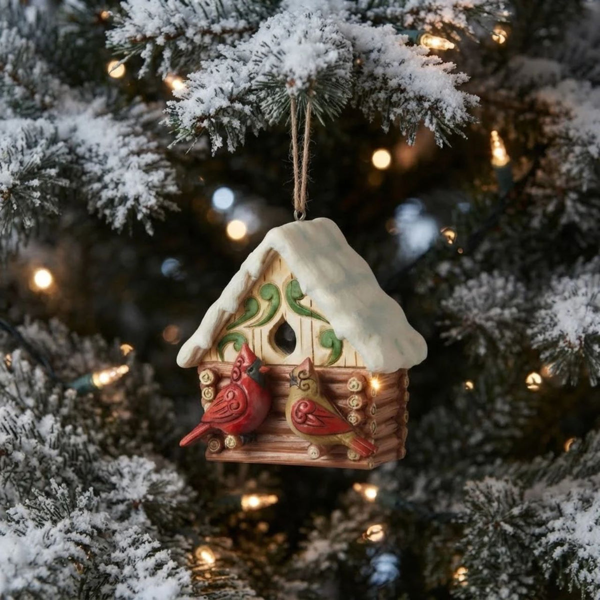 This Christmas at the Lodge enchanting Jim Shore ornament showcases a charming birdhouse designed to resemble a miniature log cabin, complete with Jim Shore's iconic rosemaling. Perched are a pair vibrant cardinals that add a touch of love.