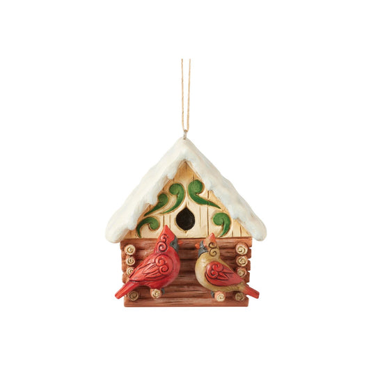 This Christmas at the Lodge enchanting Jim Shore ornament showcases a charming birdhouse designed to resemble a miniature log cabin, complete with Jim Shore's iconic rosemaling. Perched are a pair vibrant cardinals that add a touch of love.