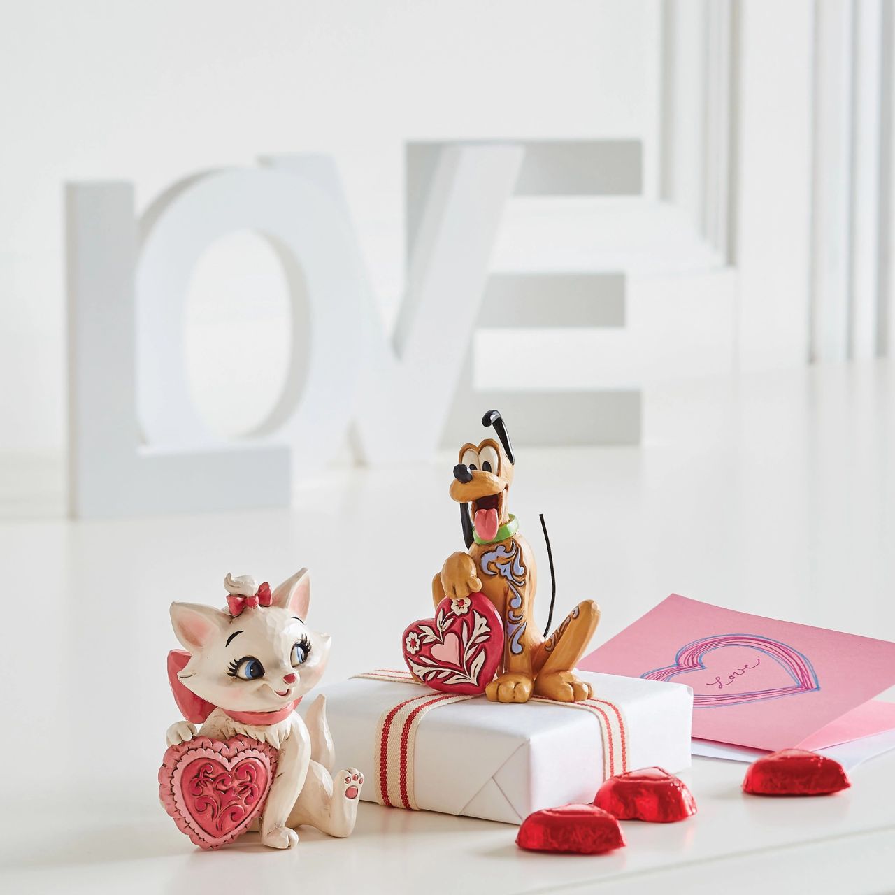 Jim Shore The Aristocats Marie Heart Mini Figurine  The 1970 Walt Disney classic, The Aristocats, followed three kittens and their mother across the Parisian countryside after being cat-napped from their home. Marie, the only daughter of the bunch, holds a pink heart in this sweet Jim Shore figurine. Packaged in a branded gift box.