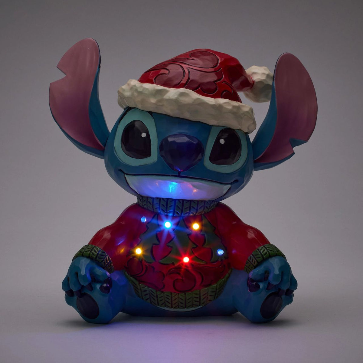 Stitch brings holiday humour to life in this glowing Jim Shore bust with an LED lit Christmas sweater. Wearing his sweater and Santa hat with a smile, the mischievous alien proves holiday magic spans across the universe with festive folk art style.