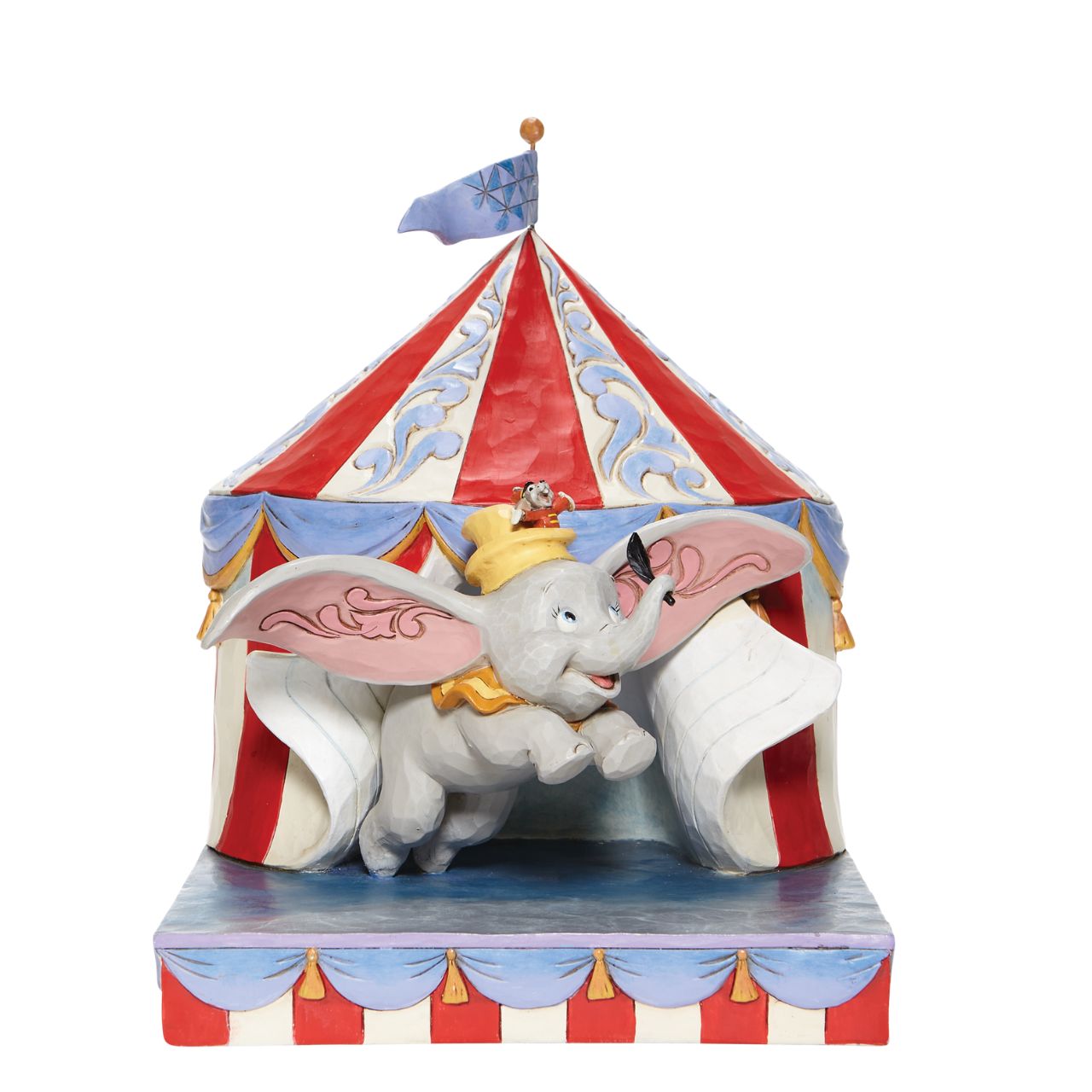 Jim Shore Over the Big Top - Dumbo Circus out of Tent Figurine  With Timothy's encouragement, guidance, and the willingness from a feather, Dumbo takes his favourite friend on an adventurous flight. This Disney piece by Jim Shore is intricately hand-painted and detailed with folk art motifs and is great for any Dumbo fan.