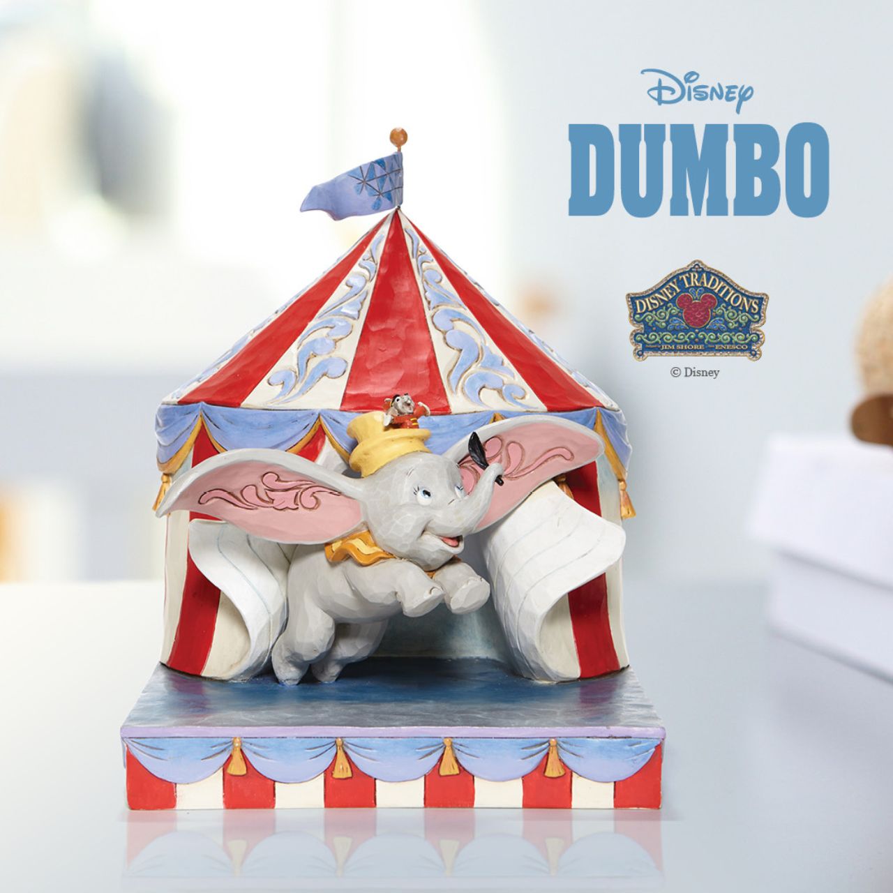 Jim Shore Over the Big Top - Dumbo Circus out of Tent Figurine  With Timothy's encouragement, guidance, and the willingness from a feather, Dumbo takes his favourite friend on an adventurous flight. This Disney piece by Jim Shore is intricately hand-painted and detailed with folk art motifs and is great for any Dumbo fan.