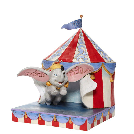 Jim Shore Over the Big Top - Dumbo Circus out of Tent Figurine  With Timothy's encouragement, guidance, and the willingness from a feather, Dumbo takes his favourite friend on an adventurous flight. This Disney piece by Jim Shore is intricately hand-painted and detailed with folk art motifs and is great for any Dumbo fan.