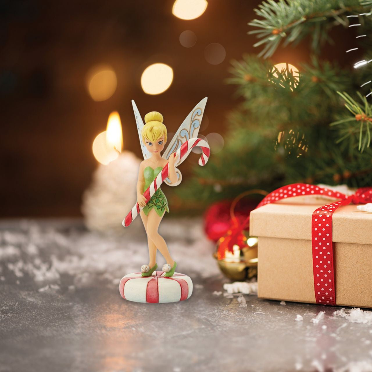 In this enchanting Jim Shore design, Tinker Bell stands atop a vibrant peppermint, delicately holding a candy cane with a sweet smile that radiates holiday warmth. Her enchanting presence brings a touch of pixie dust and magic to the holiday season.