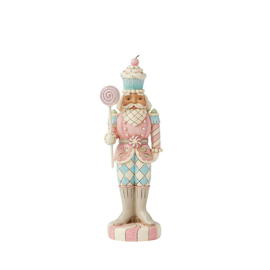 This Heartwood Sweets toy soldier design by Jim Shore stands proudly on a peppermint base, holding a lollipop staff. With a pastel-patterned uniform of icing and gumdrops, complete with a peppermint belt buckle and a delightful cupcake hat, he brings sweet presence to any holiday scene.